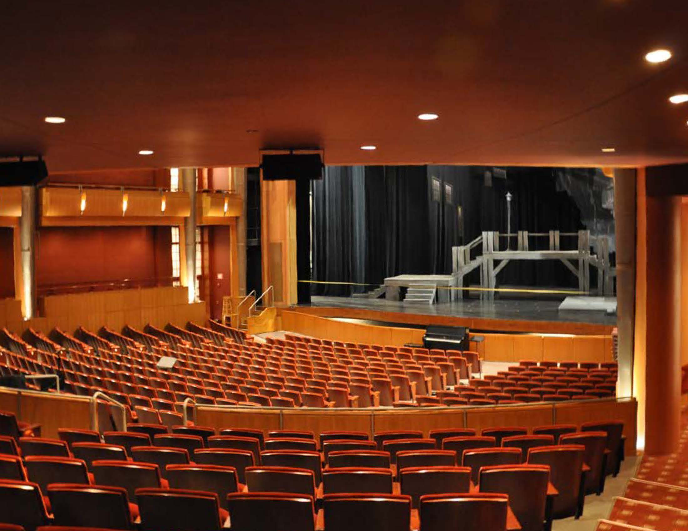 Empty theater auditorium with rows of seats facing a stage set.